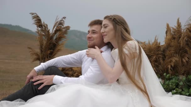 Молодая женщина в свадебном платье обнимает мужчину и пара смеется — стоковое видео