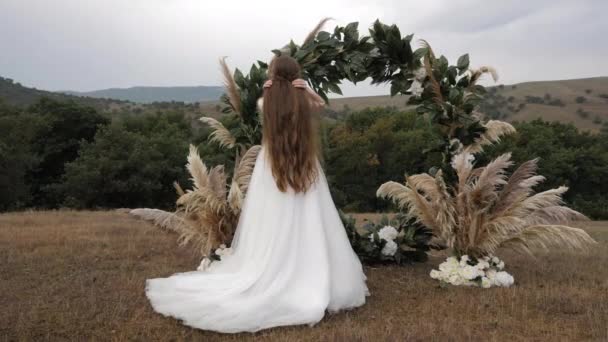 Дама в весільній сукні фіксує вільне волосся, що тече біля арки — стокове відео