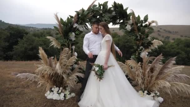 Hombre guapo abraza atractiva dama en vestido de novia en arco — Vídeos de Stock