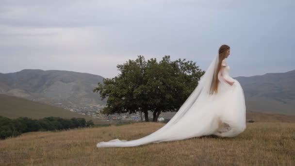 Brunette in long white wedding dress runs along meadow — 图库视频影像
