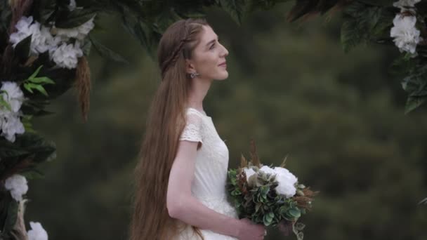 Pretty long haired bride stands under decorated wedding arch — Stok video