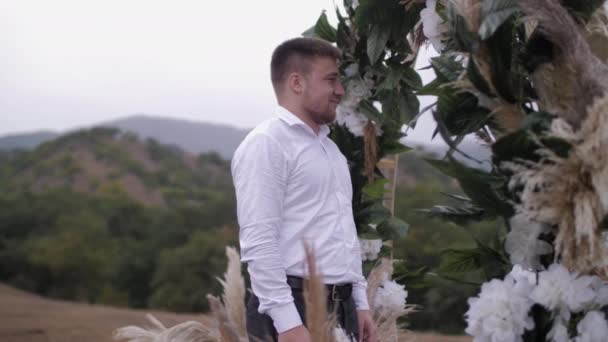 Smiling fiance stands under decorated wedding venue arch — Stockvideo