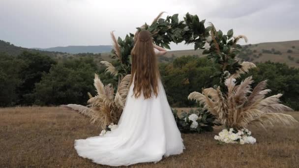 Νύφη με μακριά χαλαρά μαλλιά στέκεται κοντά αψίδα γάμου — Αρχείο Βίντεο