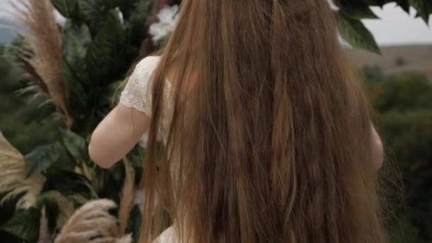 Bride in dress straightens long loose flowing hair near arch — 비디오