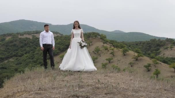 Jovem mulher em longo vestido de noiva branco caminha contra noivo — Vídeo de Stock