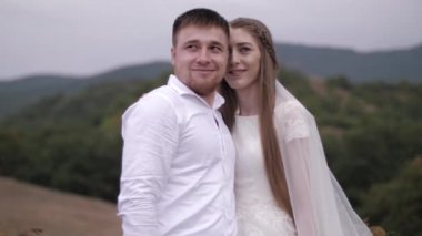 Yakışıklı adam duvağı olan beyaz gelinlikli kıza sarılıyor.