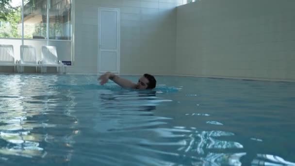 Αθλητής κολυμπά κατά μήκος πλατιάς πισίνας ενάντια σε λευκές καρέκλες — Αρχείο Βίντεο