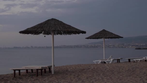 Rieten parasols in de buurt van witte ligstoelen op zandstrand in de ochtend — Stockvideo