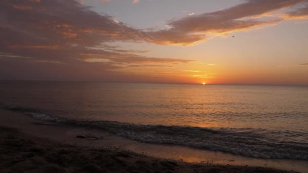 Olas del océano rodar en la playa de arena contra la puesta de sol naranja brillante — Vídeo de stock