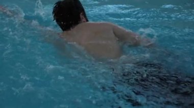 Siyah saçlı sporcu mavi yüzme havuzu boyunca yüzer.
