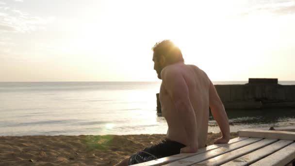 肌肉男在木制长椅上对着大海运动 — 图库视频影像