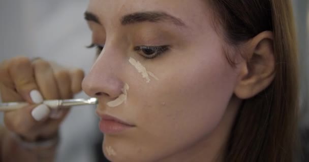 Salon piękności mistrz wyrównuje korektor na atrakcyjnej twarzy dziewczyny — Wideo stockowe