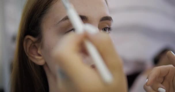 Make-up kunstenaar uitlijnt concealer op jonge vrouw gezicht closeup — Stockvideo