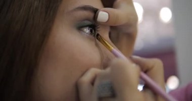 Visagiste, genç bir kadının yüzüne yakından yeşil göz farı sürüyor.