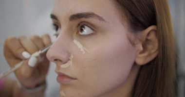 Profesyonel güzellik salonu çalışanı yumuşatıcısı kadın yüzüne saklayıcı sürmüş.