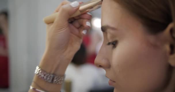 Artista de maquiagem aplica corretor no rosto modelo atraente — Vídeo de Stock