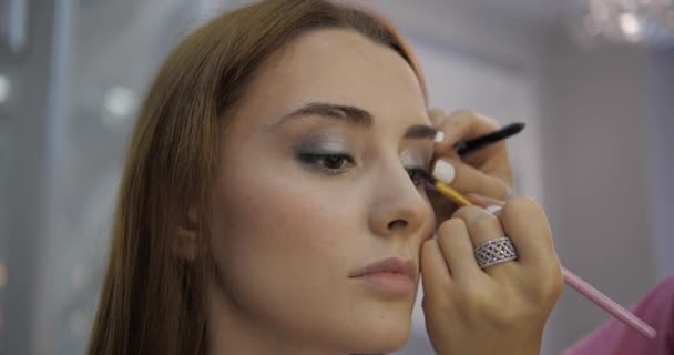 Визажисты наносят тени для век на глаза молодой женщины — стоковое видео