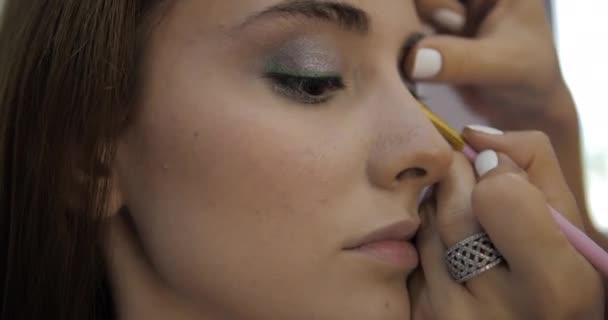 Makeup artist draws arrows on attractive young woman face — Stock video