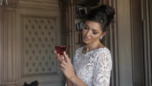 Brunette in wit lacy trouwjurk kijkt naar rood wijnglas — Stockvideo