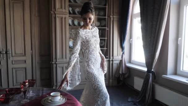 Lady in long white lacy tight wedding dress walks about room — Stock video