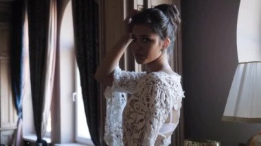 young woman in white dress poses holding hand on hairstyle