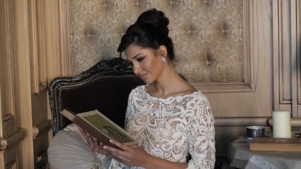 Приваблива брюнетка сидить у старовинному кріслі і читає книгу — стокове відео