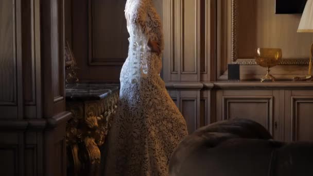 Slim woman in long white lacy dress poses near table — Αρχείο Βίντεο