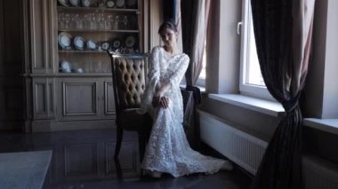 attractive brunette in long white lacy dress sits on chair