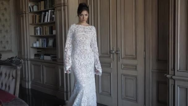 Красивая невеста в длинном белом кружевном платье ходит по комнате — стоковое видео