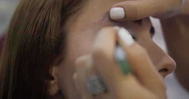 Artista de maquiagem desenha seta verde na sobrancelha modelo bonita — Vídeo de Stock