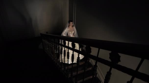 Wonderful bride in white wedding dress stands on dark stairs — ストック動画