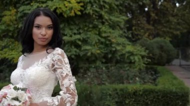 Dantelli gelinlik ve parkta buketi olan pozitif gelin.