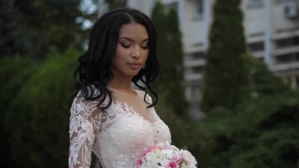 Positive bride in lacy wedding dress holds flowers by park — Stock Video