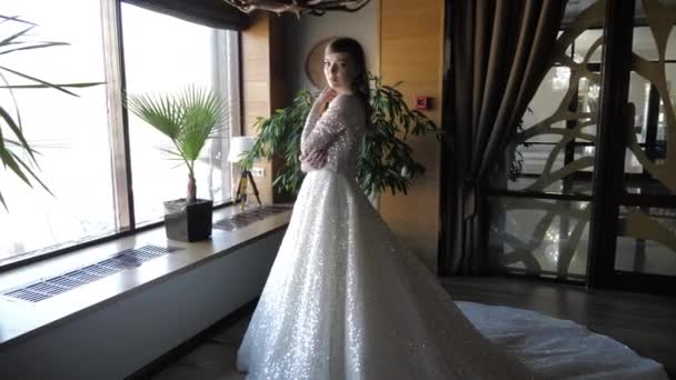 Elegant brud i bröllopsklänning poser stående nära fönstret — Stockvideo