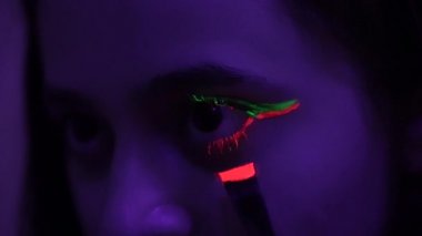 Genç bir kadın turuncu neon maskarasını dikkatle gözlerine sürüyor.