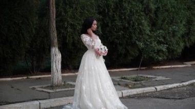 Gelinlikli güzel kız Park 'ın yanında buketle poz veriyor.