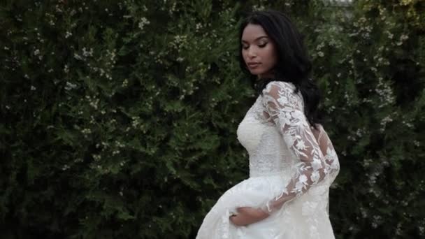 Langhaarige Braut im Spitzenhochzeitskleid spaziert im grünen Park — Stockvideo