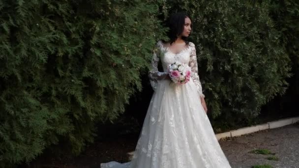 Young woman in wedding dress holds bouquet in green park — Stock Video