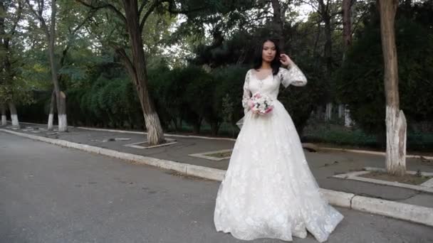 Elegant bride in lacy white dress holds bouquet near park — Stock Video