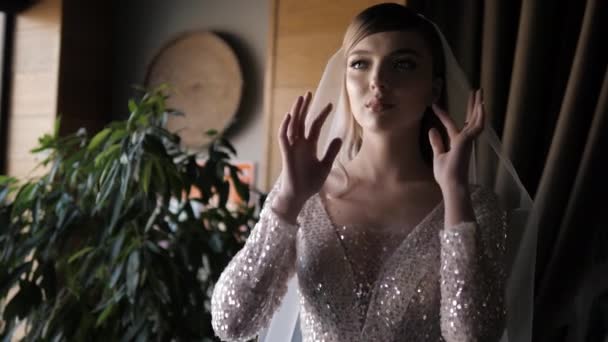 Bride in wedding dress with Swarovski crystals touches veil — Stock video