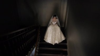 lighted bride walks down dark stairs holding shining dress