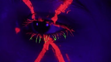 person eye with red cross and green neon mascara closeup