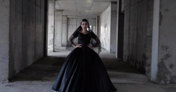 長い黒のドレスの女性は放棄された建物に沿って歩き — ストック動画