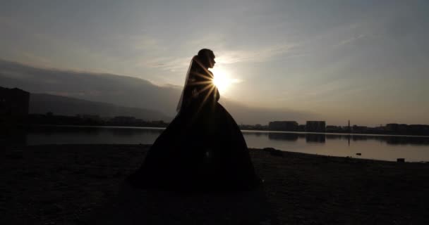 Amazon in jurk met sluier silhouet staat in de buurt van rustige meer — Stockvideo