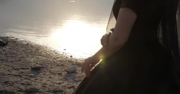 Genç bir kadın, sakin suyun yanında durarak elbisesinin üzerinde ellerini çalıştırıyor. — Stok video
