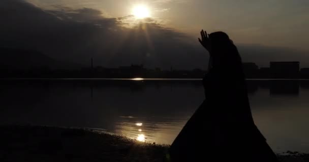 Jovem mulher no vestido levanta mão escondendo rosto de pôr do sol — Vídeo de Stock