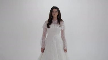 Beyaz gelinlikli uzun saçlı esmer kamera için poz veriyor.