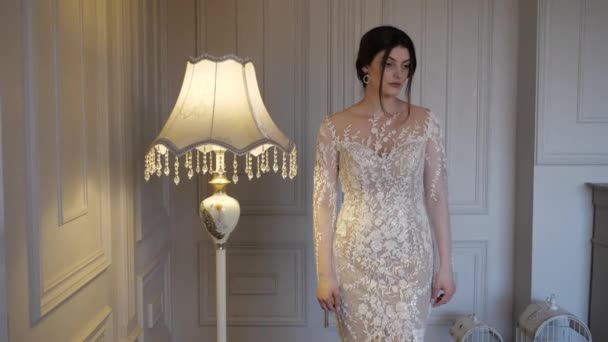 Романтическая брюнетка в длинном белом кружевном платье стоит рядом с лампой — стоковое видео