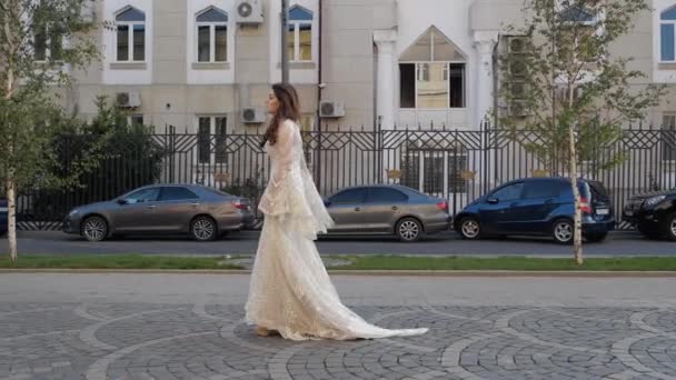 Модель в платье с длинными кружевными рукавами проходит мимо здания — стоковое видео