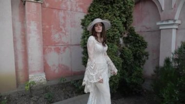 Dar gelinlikli, uzun saçlı esmer ve beyaz şapkalı.